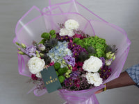 Bouquet of flowers with a pink wrap held by a person, against a neutral background.